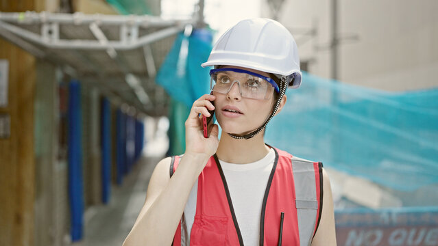 Young beautiful hispanic woman builder talking on smartphone at street