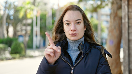 Young caucasian woman standing with serious expression saying no with finger at park