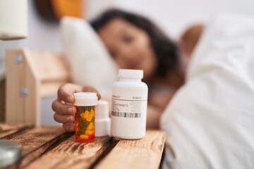 Young woman lying on bed holding pills bottle at bedroom