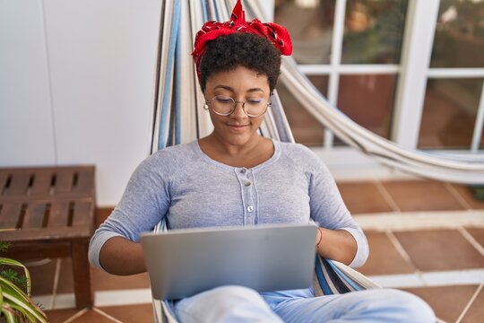 African american woman using laptop lying on hammock at home terrace