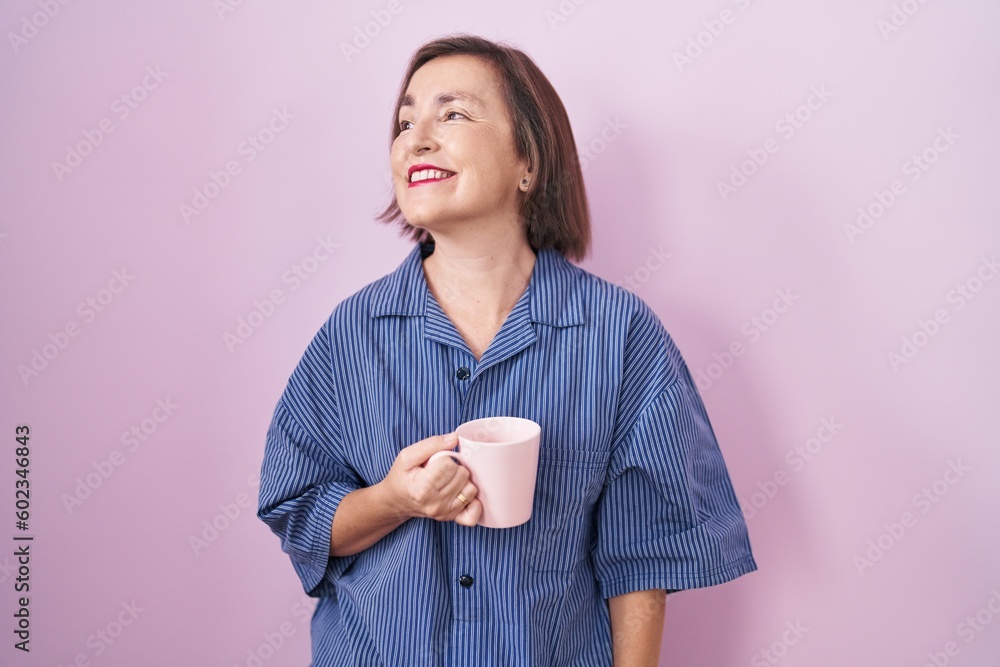 Wall mural middle age hispanic woman drinking a cup coffee looking away to side with smile on face, natural exp