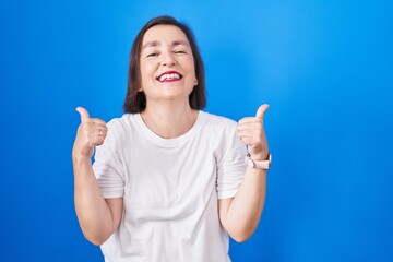Fototapeta premium Middle age hispanic woman standing over blue background success sign doing positive gesture with hand, thumbs up smiling and happy. cheerful expression and winner gesture.