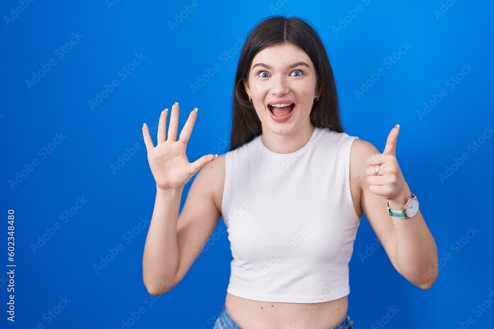 Sticker Young caucasian woman standing over blue background showing and pointing up with fingers number six while smiling confident and happy.