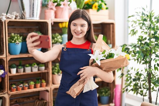 Young caucasian woman florist make selfie by smartphone holding flowers at florist