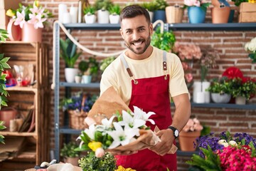 Young hispanic man florist holding bouquet of flowers at florist