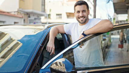 Young hispanic man smiling confident leaning on car door at street