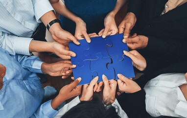 Diverse corporate officer workers collaborate in office, connecting puzzle pieces to represent partnership and teamwork. Unity and synergy in business concept by merging jigsaw puzzle. Concord - obrazy, fototapety, plakaty