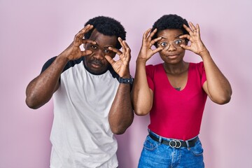 Young african american couple standing over pink background trying to open eyes with fingers, sleepy and tired for morning fatigue