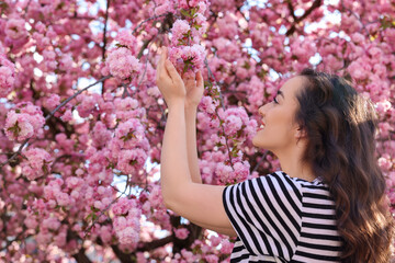 Fototapeta premium Beautiful woman near blossoming sakura tree on spring day