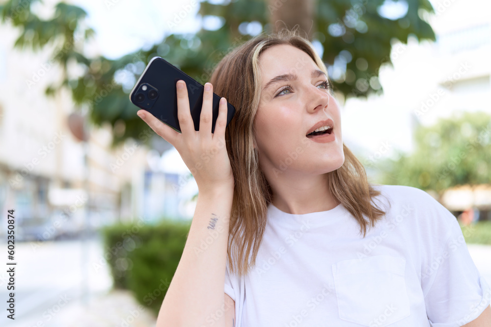 Wall mural Young caucasian woman smiling confident listening audio message by the smartphone at street