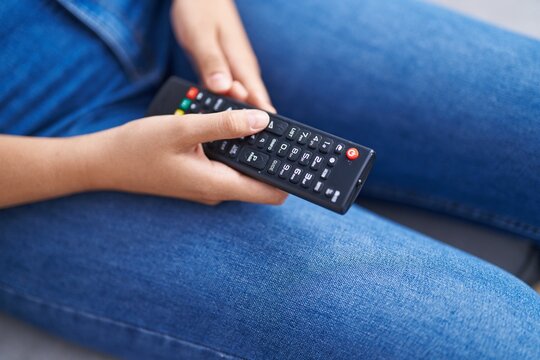Young beautiful hispanic woman using tv remote control sitting on sofa at home