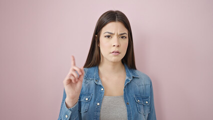 Young beautiful hispanic woman saying no with finger over isolated pink background