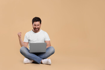 Emotional man with laptop on beige background. Space for text