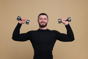 Fototapeta na wymiar Handsome sportsman exercising with dumbbells on brown background