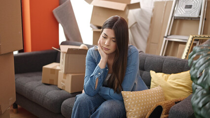 Young beautiful hispanic woman sitting on sofa with unhappy expression at new home