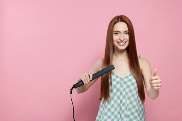 Beautiful woman using hair iron and showing thumbs up on pink background, space for text