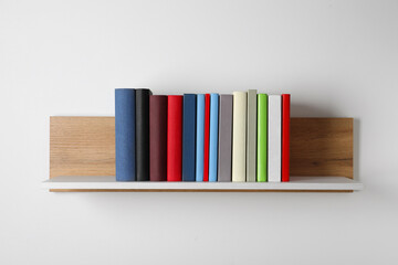 Many hardcover books on wooden shelf near white wall