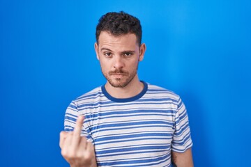 Young hispanic man standing over blue background showing middle finger, impolite and rude fuck off...