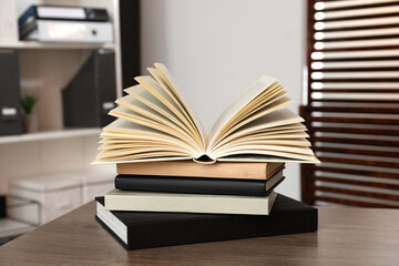Stack of different hardcover books on wooden table indoors