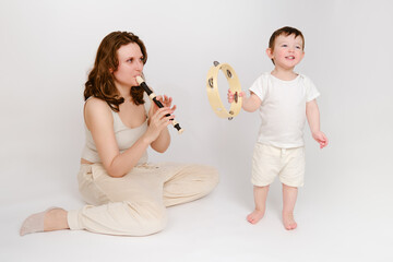 Happy baby with mother play musical instruments on studio white background. Portrait of a smiling...