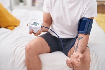 Young hispanic man measuring pulse using tensiometer at bedroom