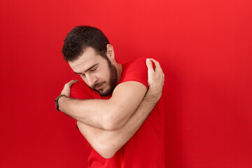 Young hispanic man wearing casual red t shirt hugging oneself happy and positive, smiling confident. self love and self care