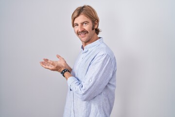 Caucasian man with mustache standing over white background pointing aside with hands open palms...