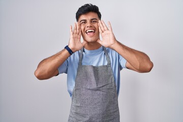 Hispanic young man wearing apron over white background smiling cheerful playing peek a boo with hands showing face. surprised and exited