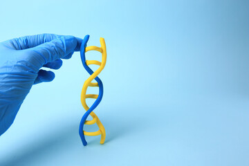 Scientist with DNA molecule model made of plasticine on light blue background, closeup. Space for...