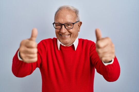 Senior man with grey hair standing over isolated background approving doing positive gesture with hand, thumbs up smiling and happy for success. winner gesture.