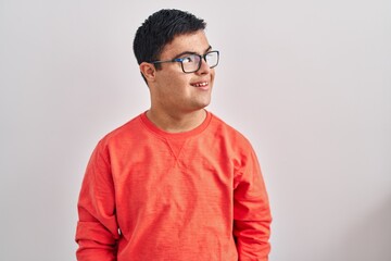 Young hispanic man with down syndrome standing over white background looking to side, relax profile...