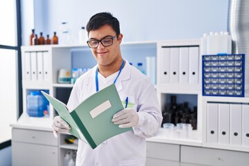 Down syndrome man wearing scientist uniform reading notebook at laboratory