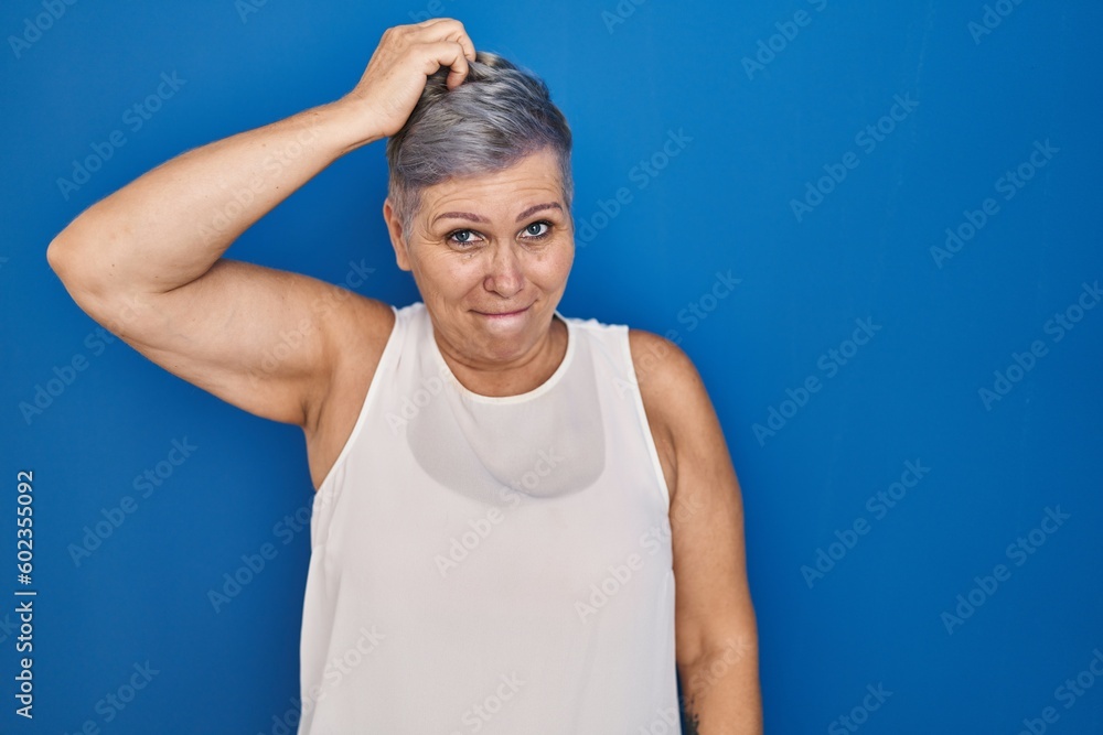 Sticker Middle age caucasian woman standing over blue background confuse and wonder about question. uncertain with doubt, thinking with hand on head. pensive concept.