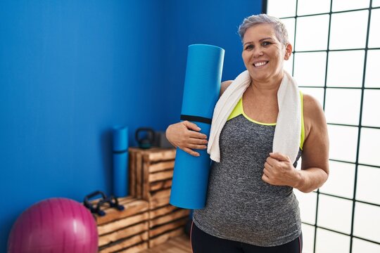 Middle age woman wearing sportswear holding yoga mat at sport center