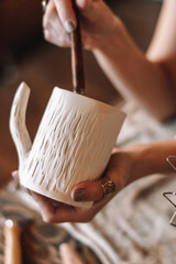 Female sculptor making clay pottery in a home workshop,glazing a clay mug,hands close-up.Small business,entrepreneurship,hobby, leisure concept.