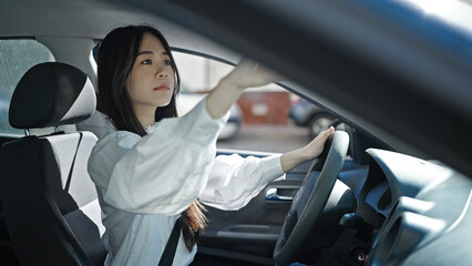 Young chinese woman touching rearview sitting on car at street
