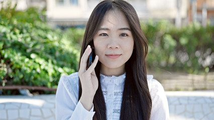 Young chinese woman talking on smartphone with serious expression at park