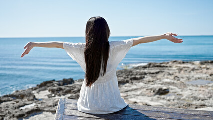 Young chinese woman sitting on bench with arms open at seaside