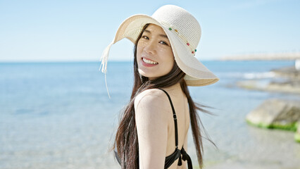 Young chinese woman tourist smiling confident wearing swimsuit and summer hat at seaside