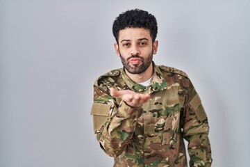 Arab man wearing camouflage army uniform looking at the camera blowing a kiss with hand on air being lovely and sexy. love expression.