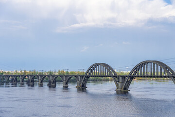 View of river Dnepr and railway ancient arched bridge. Unique construction across wide water 19th century. Railway line along the Merefo-Kherson bridge. Panoramic on modern city and spring landscape.
