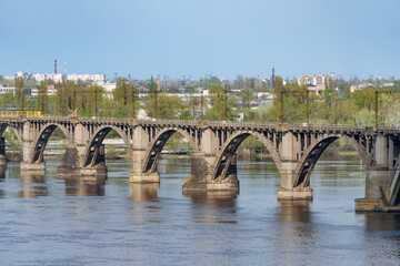 View of river Dnepr and railway ancient arched bridge. Unique construction across wide water 19th century. Railway line along the Merefo-Kherson bridge. Panoramic on modern city and spring landscape.