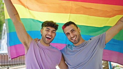 Two men couple hugging each other holding homosexual flag at park