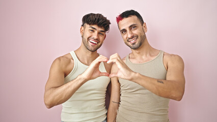 Two men couple hugging each other doing heart gesture over isolated pink background