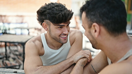 Two men couple sitting on table speaking at coffee shop terrace