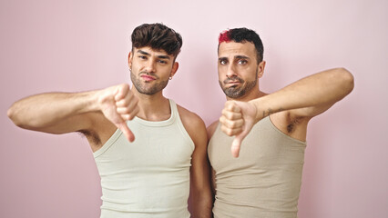 Two men couple doing negative sign with thumb down over isolated pink background © Krakenimages.com