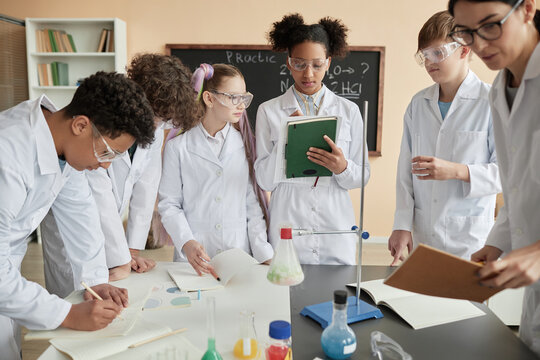 Diverse group of young teens wearing lab coats enjoying science experiments in school together