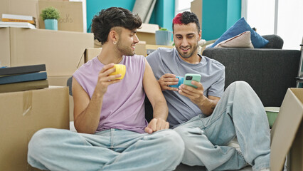 Two men couple drinking coffee using smartphone at new home