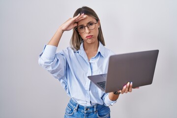 Young woman working using computer laptop worried and stressed about a problem with hand on forehead, nervous and anxious for crisis