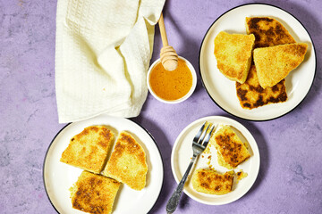hands eating a harcha or mbasses semolina algerian pancakes on an arabesque colorful plate above cutting board. Traditional algerian breakfast bread with honey bowl